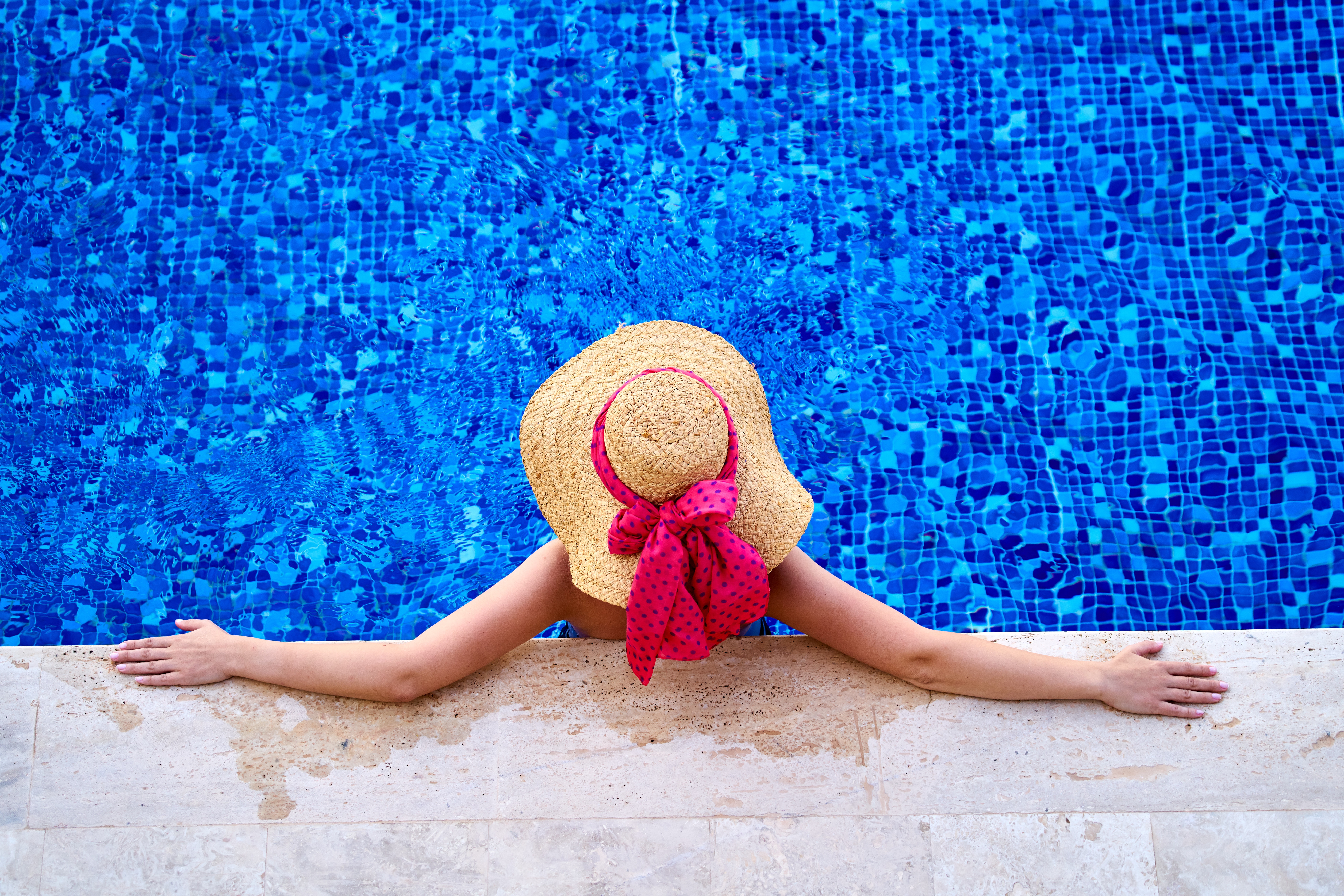 donna con cappello di paglia e fiocco rosso in piscina